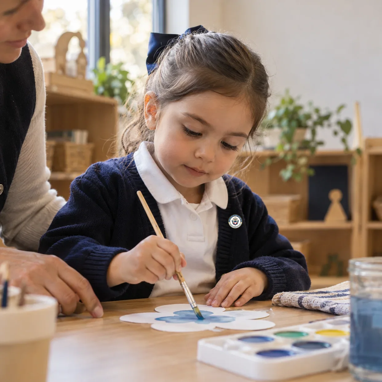 Niña de Preescolar pinta una figura de papel mientras una docente la acompaña.