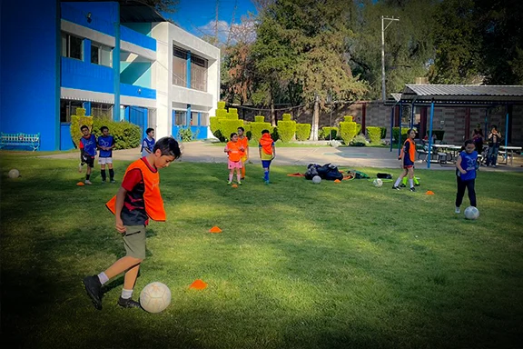 Niños practicando fútbol con balones sobre una cancha de pasto.